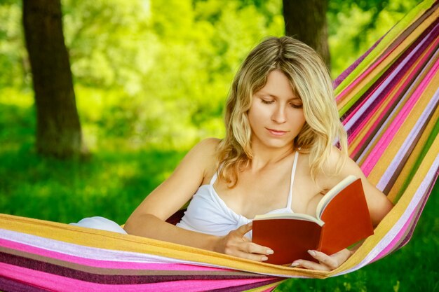 Glückliches Mädchen, das draußen im Park ein Buch in einer Hängematte liest