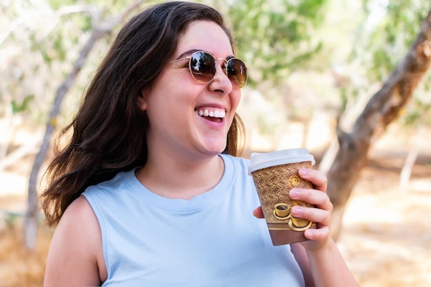 Glückliches Mädchen, das Kaffeetasse zum Mitnehmen im Freien hält