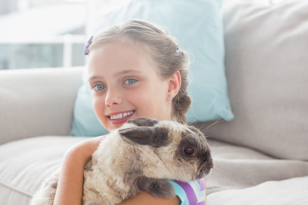 Glückliches Mädchen, das Kaninchen im Wohnzimmer hält