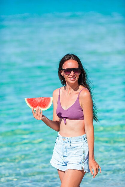 Glückliches Mädchen, das Spaß am Strand hat und Wassermelone isst
