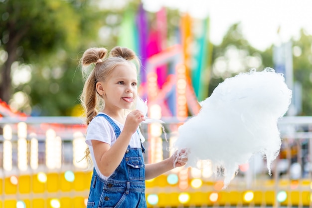 Glückliches Mädchen, das Zuckerwatte am Vergnügungspark isst