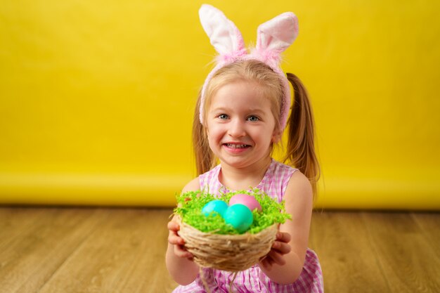 Glückliches Mädchen des blonden Kleinkindes mit Hasenohren und Eikorb für Ostern