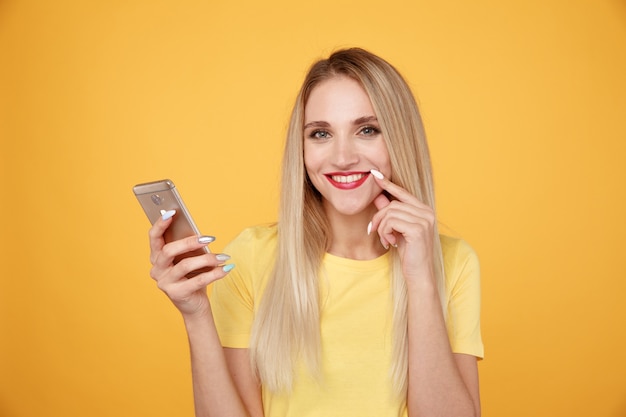 Glückliches Mädchen im gelben Studio mit dem Telefon lokalisiert.