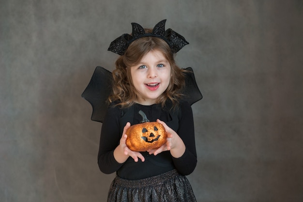 Glückliches Mädchen im Halloween-Kostüm mit Kürbis auf grauem Raum