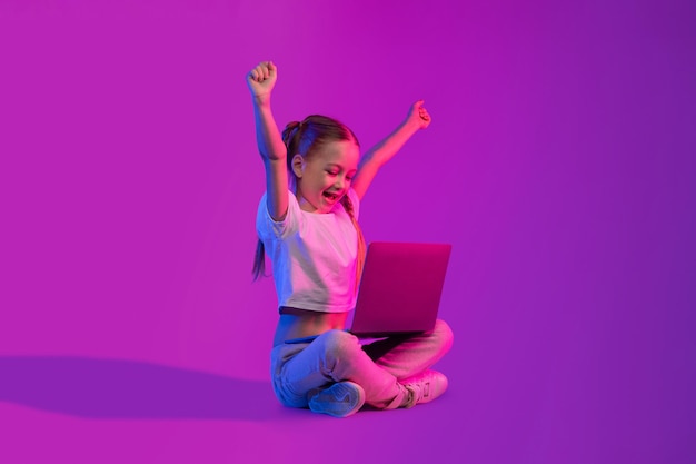Glückliches Mädchen im schulpflichtigen Alter, das Videospiele mit einem Laptop spielt