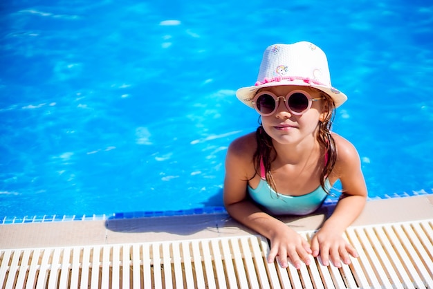 Glückliches Mädchen in der Sonnenbrille und im Hut im Außenschwimmbad von Lux