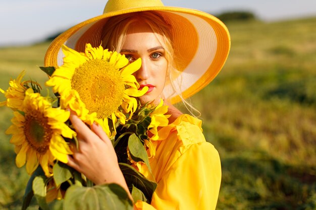 glückliches mädchen in einem gelben kleid hält sonnenblumenblumen in einem feld von sonnenblumen gegen den himmel