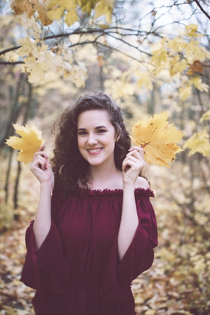 Glückliches Mädchen in einem Herbstpark, der Ahornblätter hält