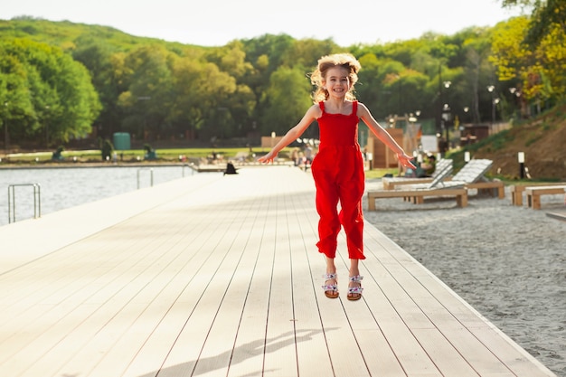 Glückliches Mädchen in einem roten Overall am Wasser, das Training macht und Spaß hat