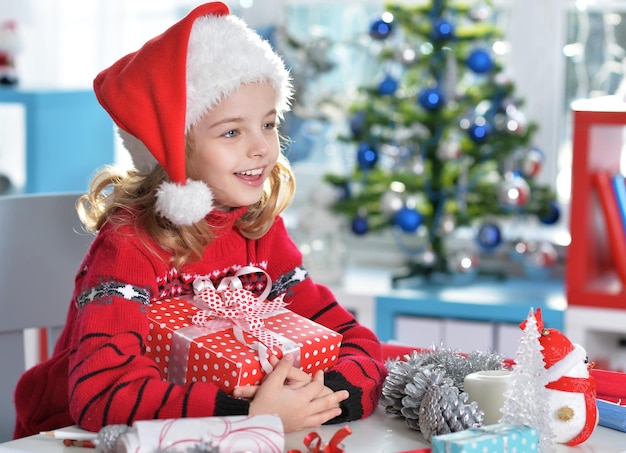 Glückliches Mädchen in Sankt-Hut, das mit Weihnachtsgeschenk sitzt