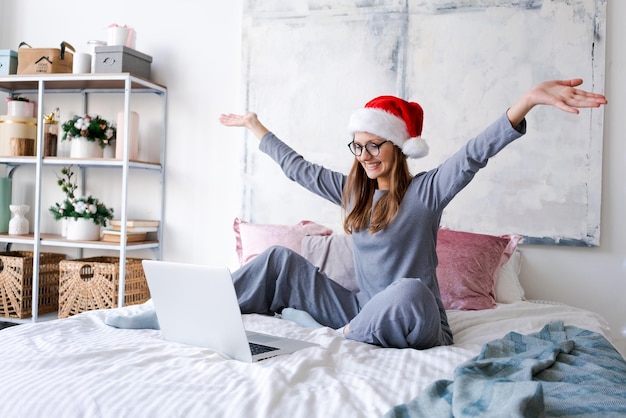 Glückliches Mädchen in Weihnachtsmütze grüßt Freunde Frohe Weihnachten Video-Chat auf dem Laptop