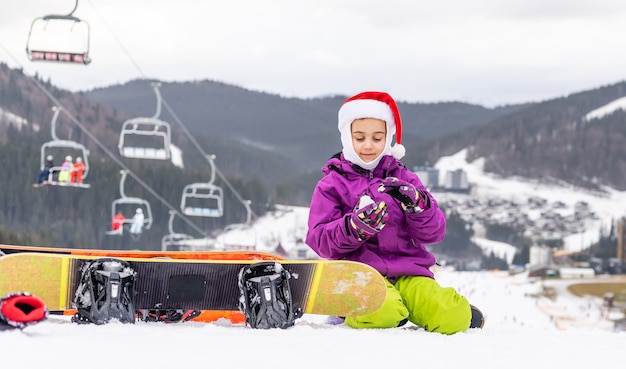 Glückliches Mädchen in Weihnachtsmütze mit Snowboard
