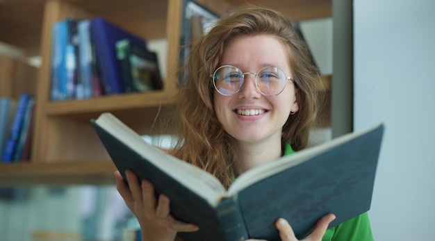 Foto glückliches mädchen, junge frau, liest buch in der bibliothek, college- oder universitätsstudentin bereitet sich mit brille auf die prüfung vor