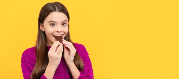 Glückliches Mädchen Kind beißen leckere Schokoladenplatte gelber Hintergrund Naschkatzen Horizontales Poster mit isoliertem Kindergesichtsbanner-Header-Kopienbereich