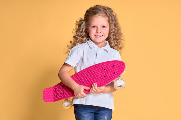 Glückliches Mädchen mit dem lockigen Haar, das Spaß mit Penny Board hat