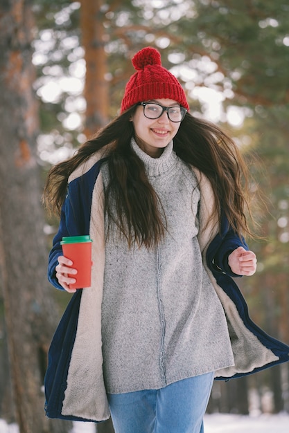 Glückliches Mädchen mit einer Tasse läuft vor der Kamera im Wald