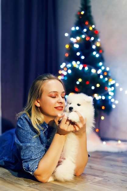 Glückliches Mädchen mit Samojede-Husky-Hund in Weihnachtsdekorationen