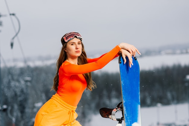 Glückliches Mädchen Snowboarder, der in Sonnenbrille mit einem Snowboard aufwirft