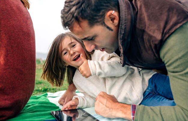 Glückliches Mädchen und ihr Vater mit Tablet, das draußen auf einer Decke liegt