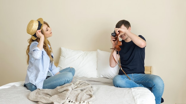 Glückliches Mädchen und Mann fotografieren sich mit alter Kamera, die in Strohmelone posiert und im Schlafzimmer lächelt