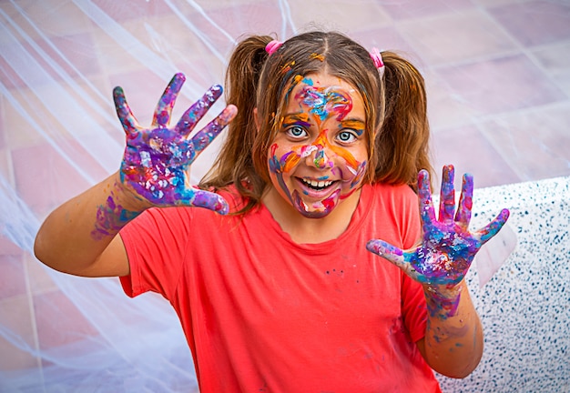 Foto glückliches mädchen wurde mit farbe verschmiert. ein kind lächelt mit leuchtenden farben auf gesicht, händen und haaren