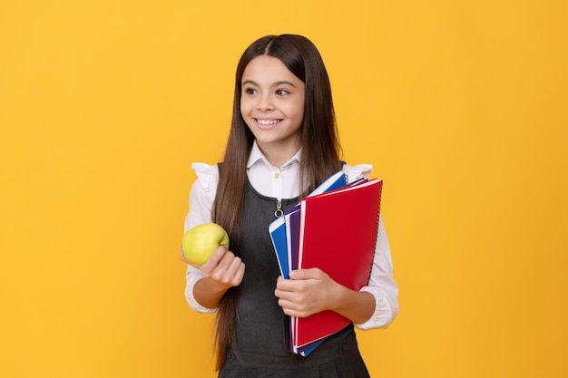 Glückliches Mädchenkind zurück zur Schule, die Apfel hält und gelben Hintergrundwissenstag bucht