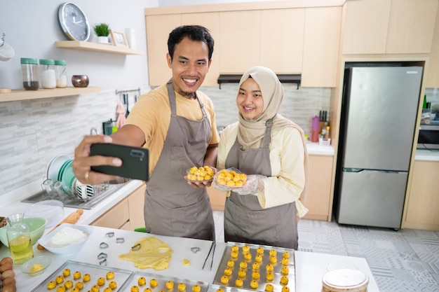 Glückliches muslimisches Paar, das selfie mit ihrem Essen macht, das zu Hause zusammen in der Küche gemacht wird. Eid Mubarak Feier Kochen