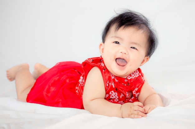 Glückliches nettes asiatisches Baby im chinesischen Traditionskleid, das im Bett lächelt und kriecht