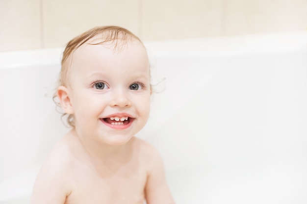 Glückliches nettes Baby im Badezimmer. Lächelndes Kind, das mit Schaum spielt.