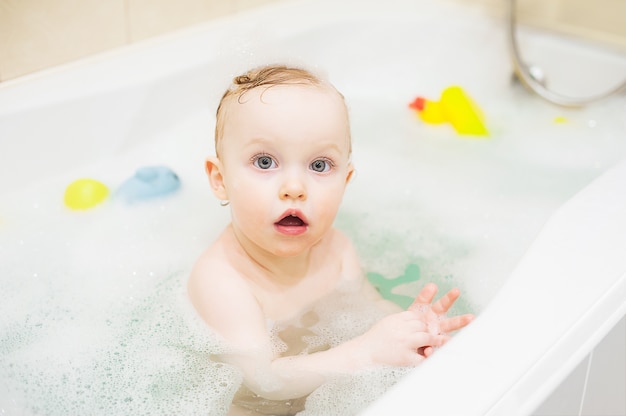 Glückliches nettes Baby im Badezimmer. Lächelndes Kind, das mit Schaumgummi und Ente spielt.