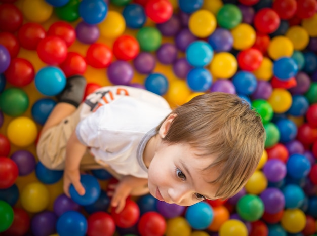 Glückliches nettes Kind, das Spaß am Kindergarten mit bunten Bällen spielt und hat