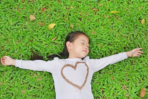 Glückliches nettes kleines asiatisches Kindermädchen, das auf grünem Rasen liegt. Lächelnd und schloss die Augen.