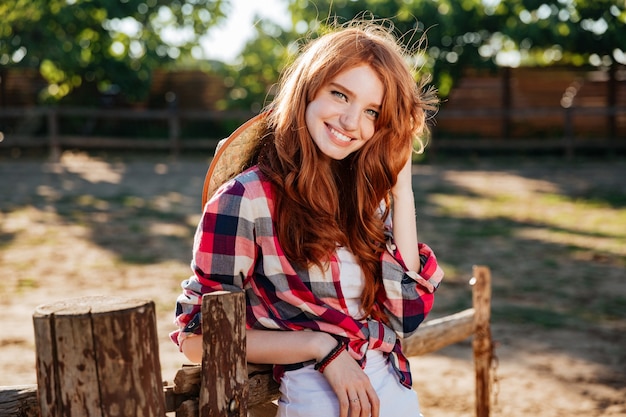 Glückliches niedliches junges Frauengowgirl, das auf Bauernhof steht und lächelt