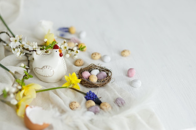 Glückliches Ostern Stilvolles Ostern Schokolade-Eier im Nest Frühlingsblumen Hühnerfiguren auf Weiß