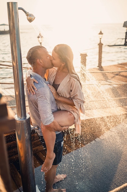 Glückliches Paar am Meer Ein Mann und ein Mädchen sind unter der Dusche auf einem Openair-Pier Glückliches Paar im Urlaub Mann und Frau am Meer