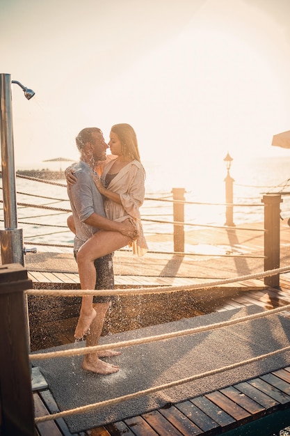 Glückliches Paar am Meer Ein Mann und ein Mädchen sind unter der Dusche auf einem Openair-Pier Glückliches Paar im Urlaub Mann und Frau am Meer