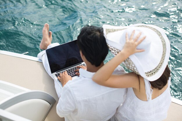 Glückliches Paar auf der Yacht mit einem Laptop