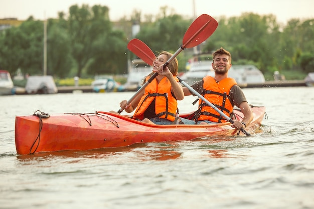 Glückliches Paar beim Kajakfahren auf dem Fluss mit Sonnenuntergang im Hintergrund