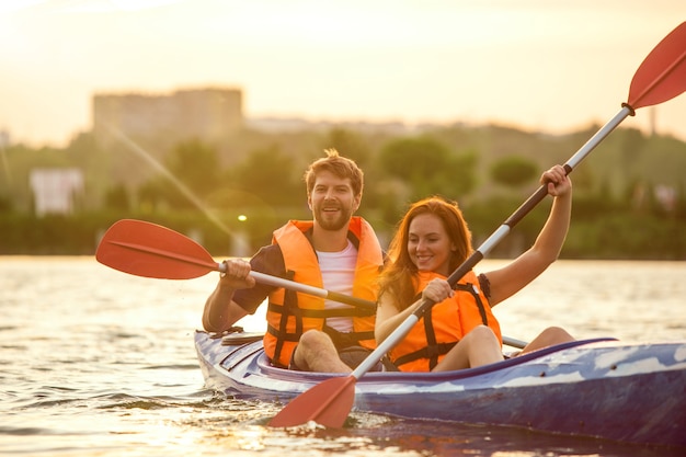 Glückliches Paar beim Kajakfahren auf dem Fluss mit Sonnenuntergang im Hintergrund