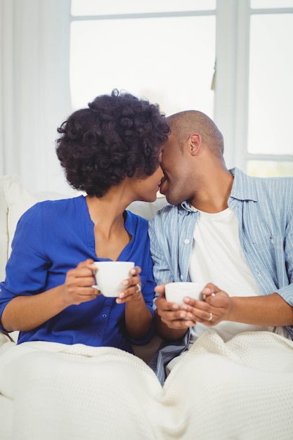 Glückliches Paar, das auf dem Sofa beim Halten von Schalen küsst