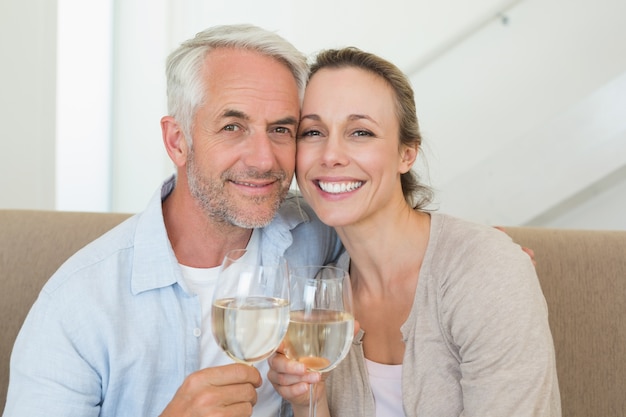 Glückliches Paar, das auf der Couch toastet mit Weißwein sitzt