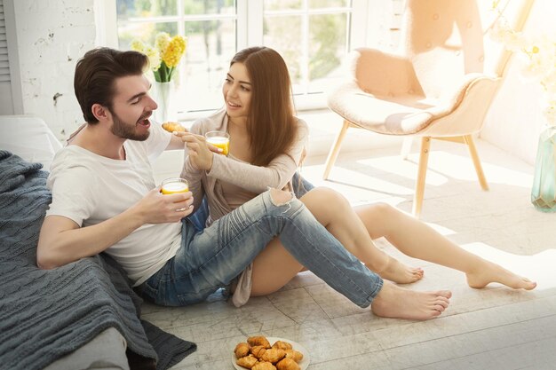 Glückliches Paar, das den Morgen zusammen im Schlafzimmer verbringt. Lässiger Mann und verliebte Frau, die auf dem Boden frühstücken, Platz kopieren