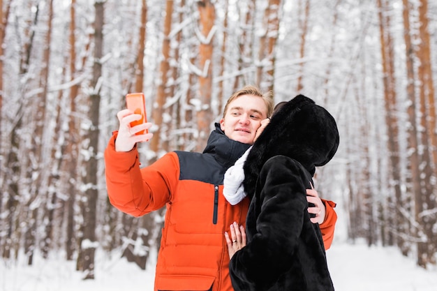 glückliches Paar, das ein Foto mit Smartphone über Winterhintergrund macht.