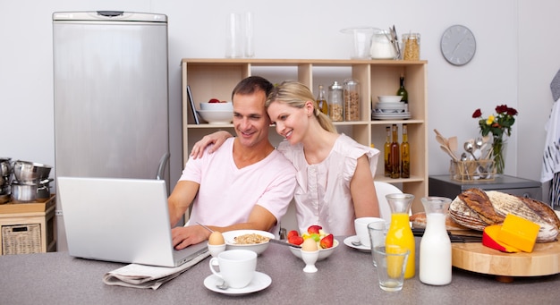 Glückliches Paar, das einen Laptop beim Frühstücken verwendet