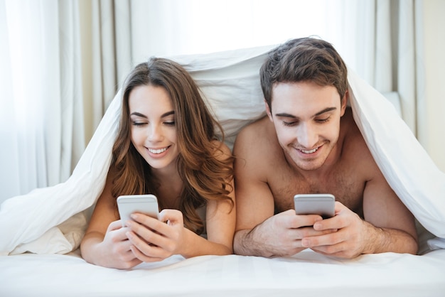 Glückliches Paar, das Handys benutzt und auf dem Bett liegt
