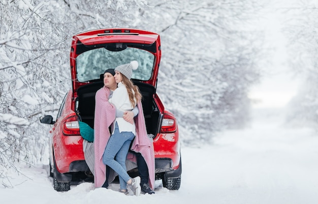 Glückliches Paar, das im offenen Auto zurück sitzt, Halt macht, Kaffee trinkt. Romantisches Reisekonzept. Winterwald.