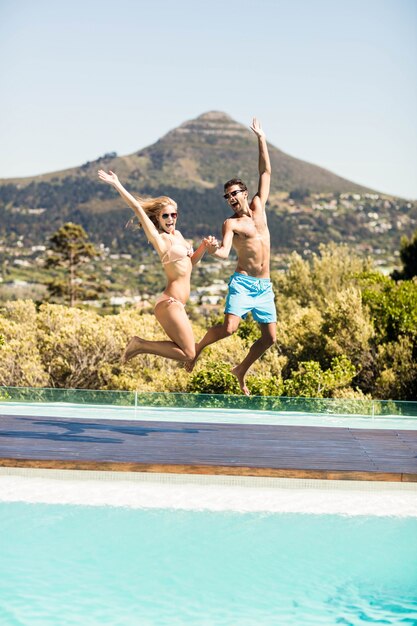 Glückliches Paar, das in das Pool an einem sonnigen Tag springt