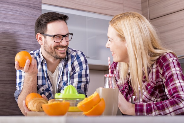 Glückliches Paar, das in der Küche natürlichen Orangensaft macht und seine Zeit genießt