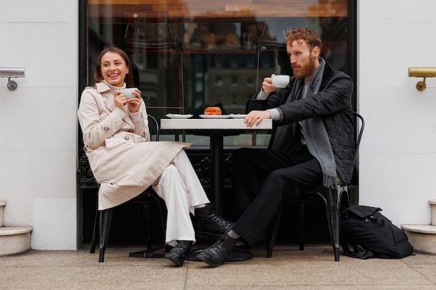 Glückliches Paar, das Kaffee trinkt und lachend miteinander redet, sitzt am Tisch eines Straßencafés auf den Straßen der Stadt
