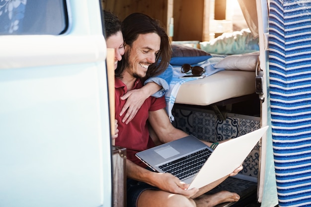 Glückliches Paar, das Laptop-Computer innerhalb Minivan während Roadtrip-Urlaub verwendet - Fokus auf Manngesicht